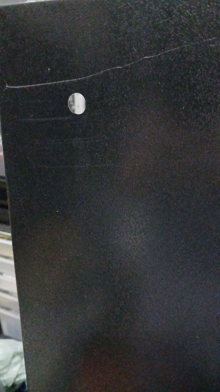 Painel preto com risco/rachadura na pintura expondo o metal, próximo a um furo de fixação.
